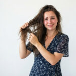 Girl standing holding her very greasy hairs due to excessive oil.