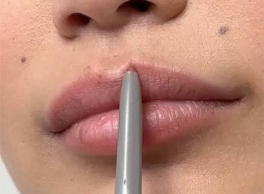 Girl applying lip liner around her lips.