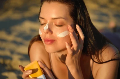 Girl applying tinted sunscreen on beach because of white caste issue.